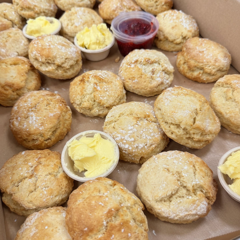 Box filled with sweet baked scones dusted with powdered sugar and several small cups of butter and jam.